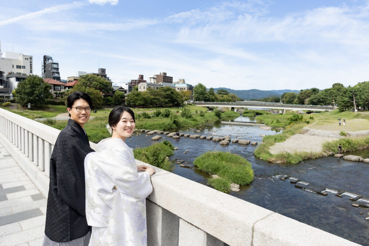 青空の鴨川の橋で前撮りする新郎新婦