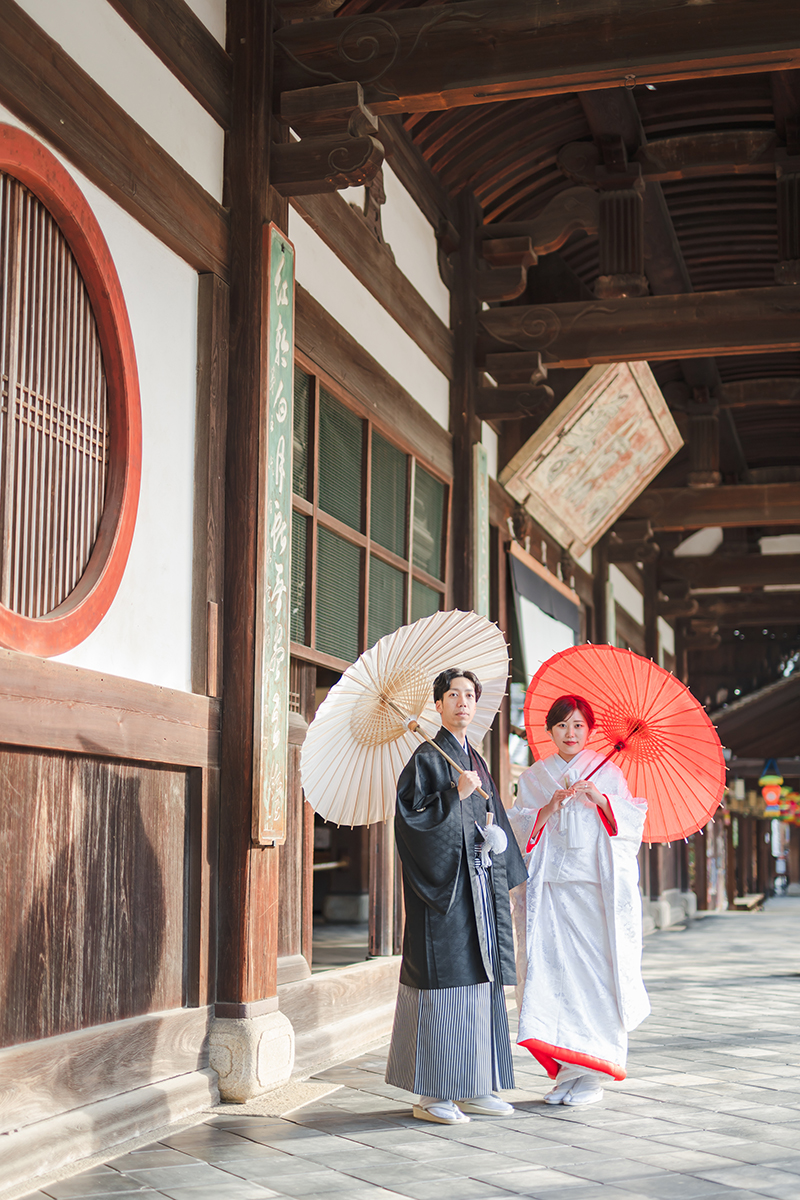 萬福寺で紅白の和傘を差す赤ふきの白無垢の新婦と黒紋付の新郎