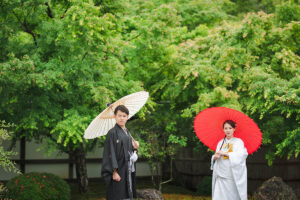 雨の日に白と赤の傘で並ぶ新郎新婦
