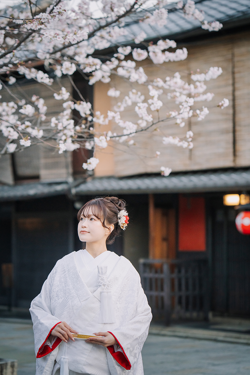 桜バックで赤ふきの白無垢を着ている新婦の美しい表情