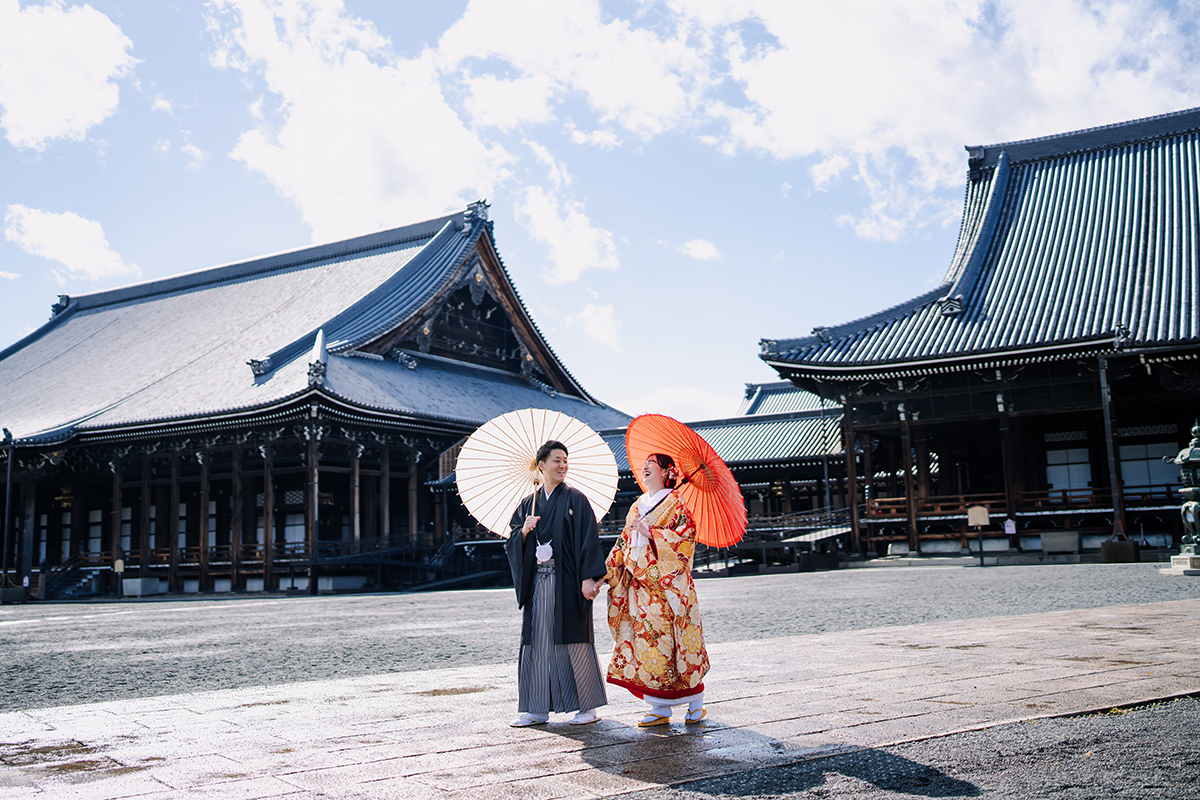 迫力あるお寺の本堂を背景に歩く新郎新婦