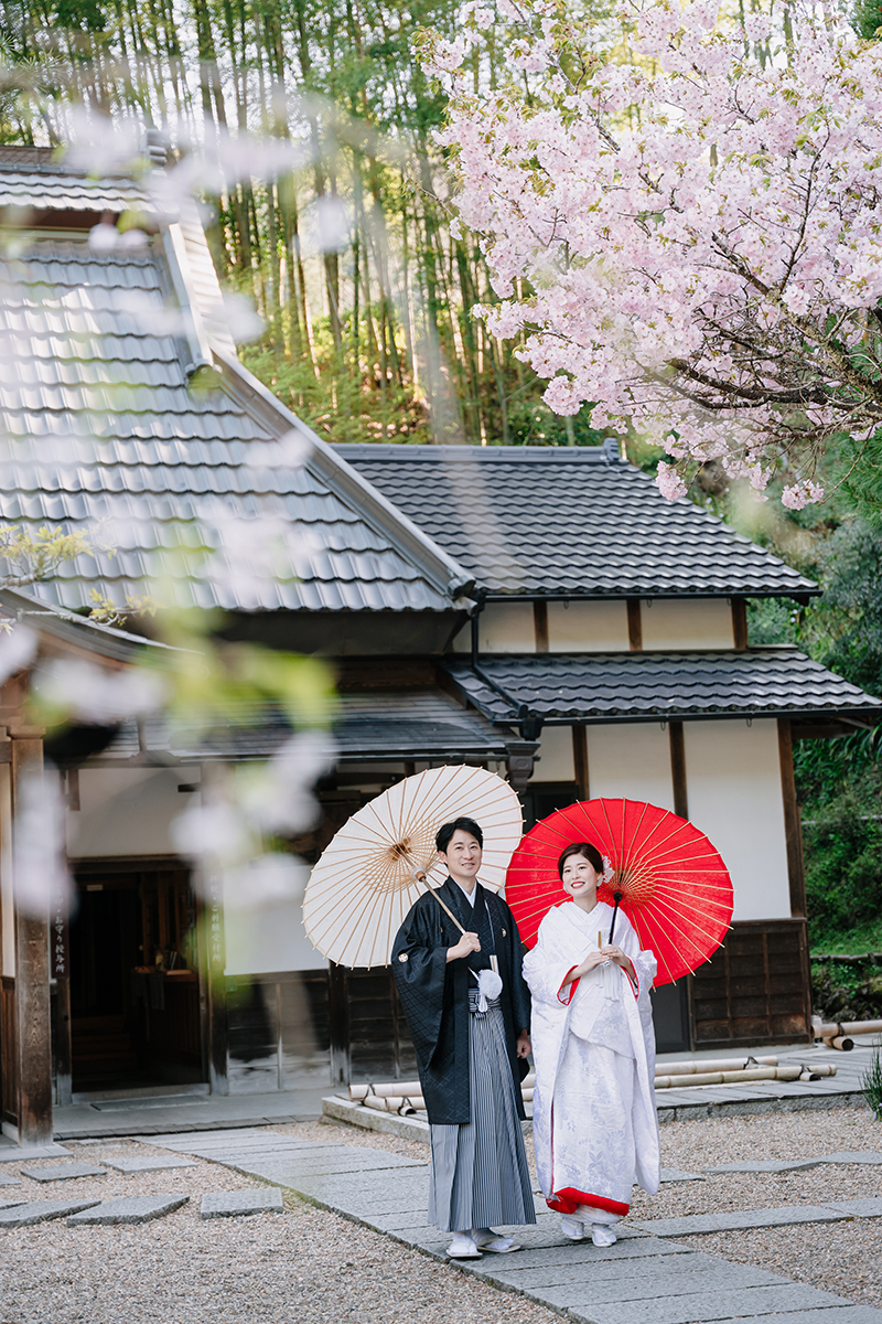 正寿院の境内で赤ふきの白無垢と黒紋付の新郎新婦が和傘を差している