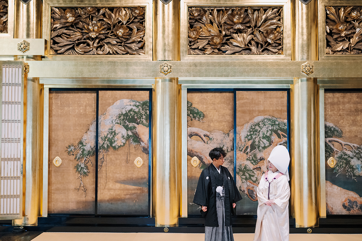 荘厳な金の襖絵の前に立つ新郎新婦