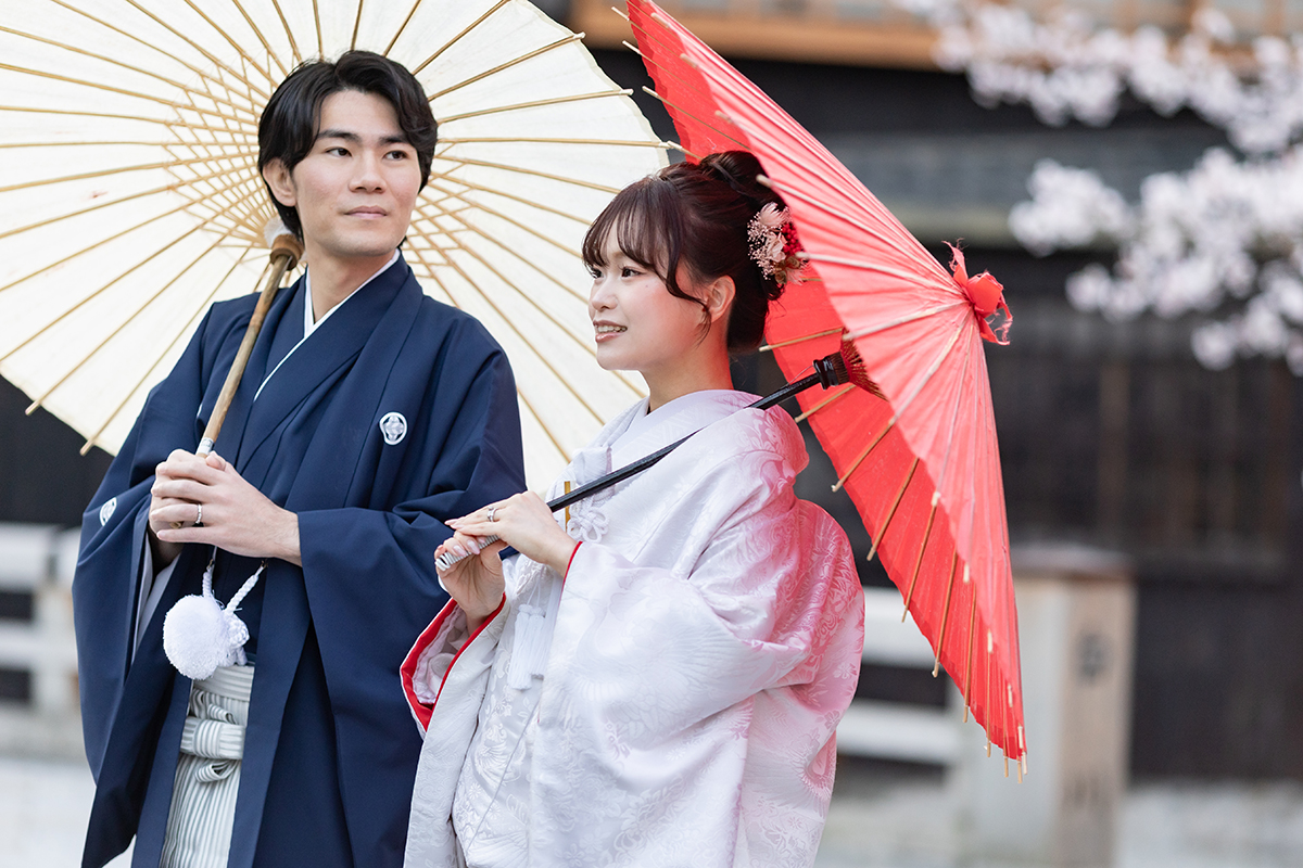 桜満開の祇園で赤ふきの白無垢姿の新婦と新郎が和傘を差している