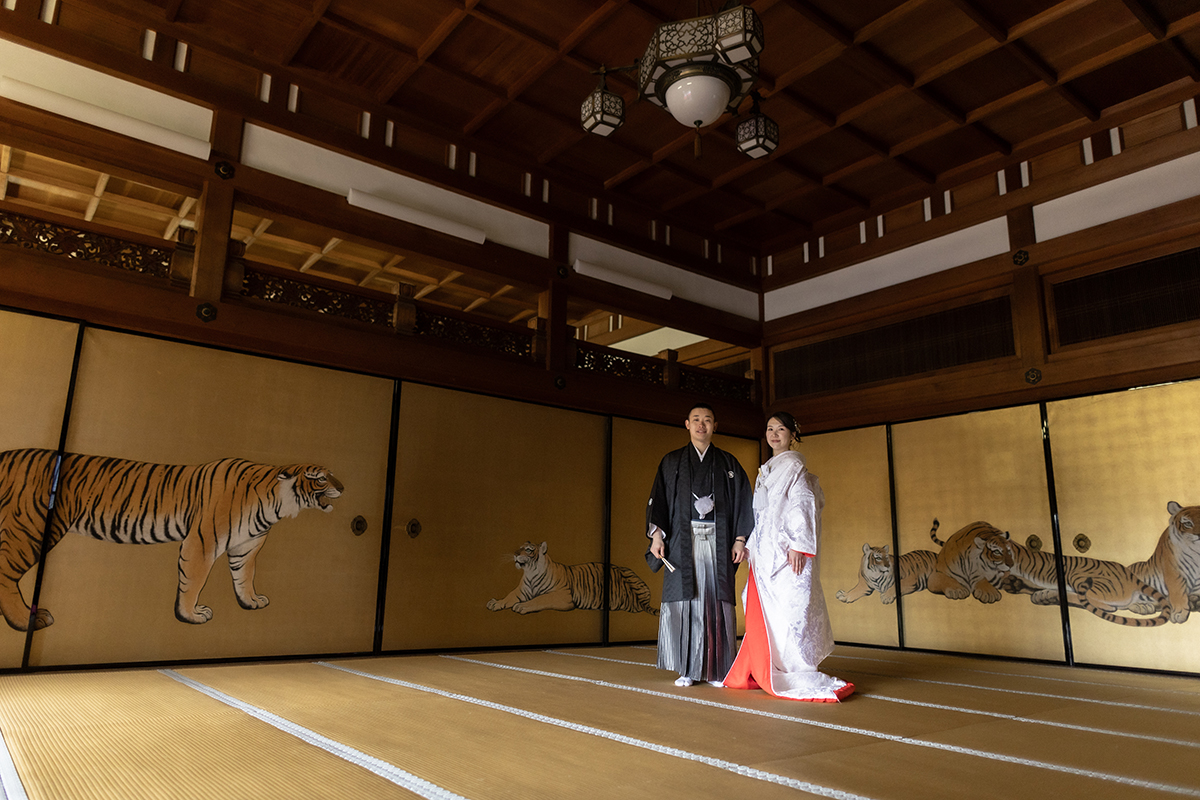 虎の襖絵の和室で赤ふきの白無垢と黒紋付姿の新郎新婦