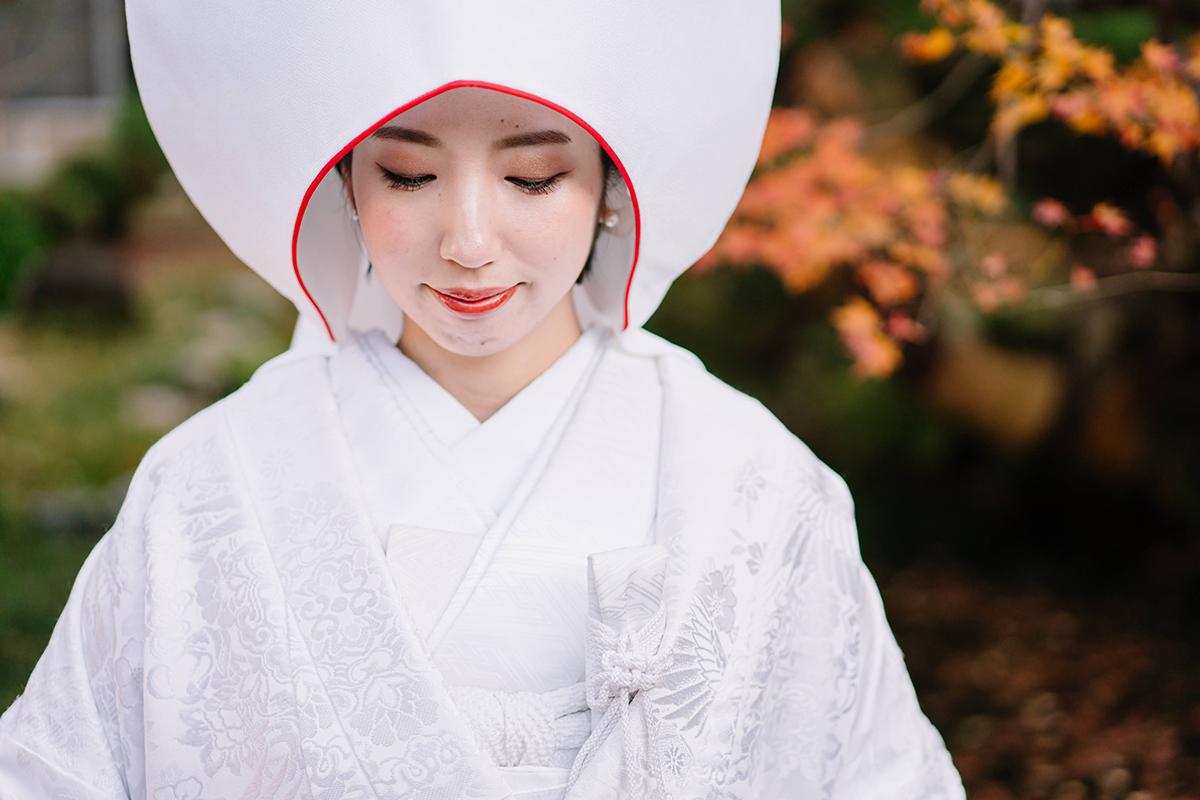 和室で赤ふきの白無垢を着て、赤こぶきの綿帽子を被ってうつむく新婦