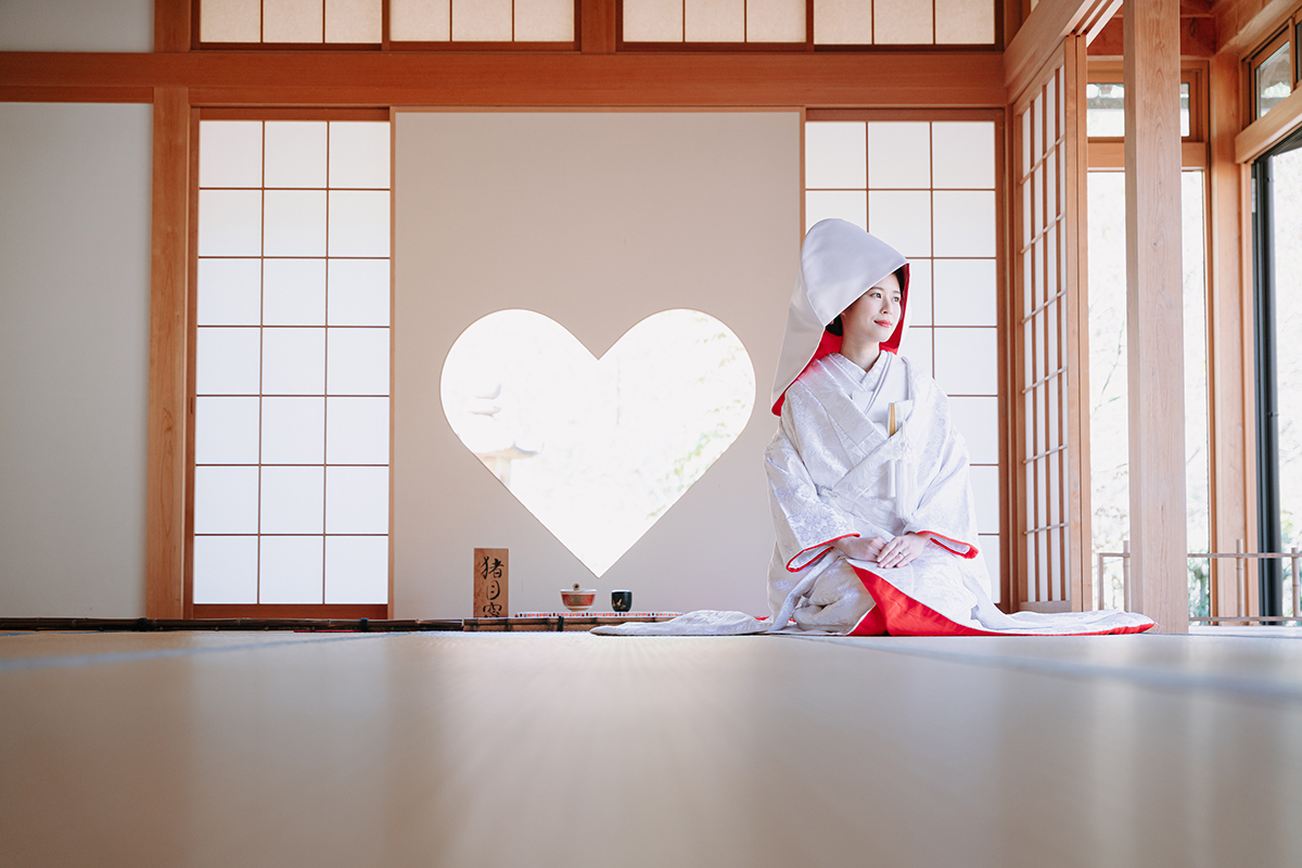 ハートの和室で赤ふきの白無垢を着て綿帽子を被って正座する新婦