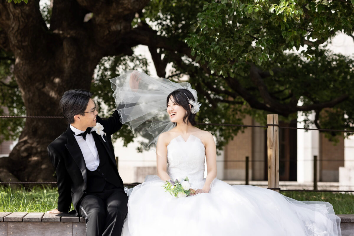京都大学の大きな楠の前のベンチで楽しそうに笑う新郎新婦
